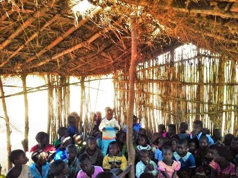 thatched roof and stick walls make the village kindergarten room and roof has a hole in it and lots of kindergarten children sitting inside