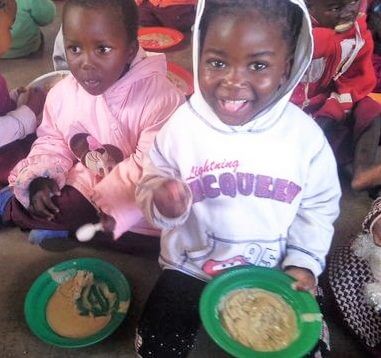 A smiling Malawian girl eating nsima at kindergarten funded by Brisbane charity Project Kindy